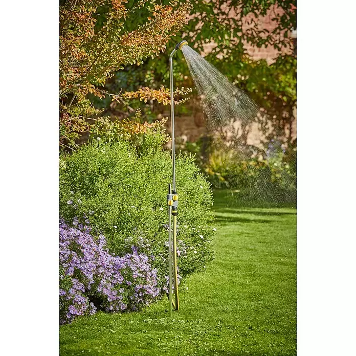 Neptun Gartendusche - 117 cm, Dreibeinstativ, Aluminium - Eine silberne Gartendusche mit schwarzem und gelbem Kopf sprüht Wasser in einen üppigen Garten. Ein gelber Schlauch ist an eine graue Armatur angeschlossen.