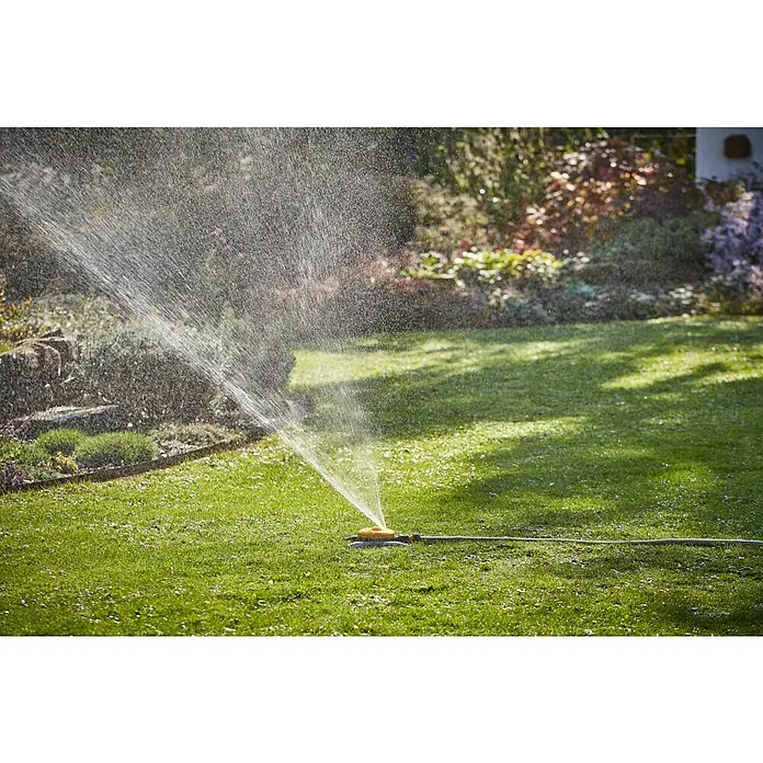 Neptun Vielflächenregner - Kunststoff - Rasensprenger in Aktion, der einen grünen Garten bewässert. Das gelbe Gerät ist mit einem grauen Schlauch verbunden und sorgt für eine gleichmäßige Verteilung.