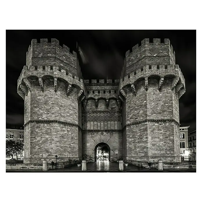 Póster Valencia Torre Serranos - An x Al: 80 x 60 cm - Puerta medieval de la ciudad en blanco y negro. Estructura monumental con almenas y un arco que enmarca un cielo oscuro.