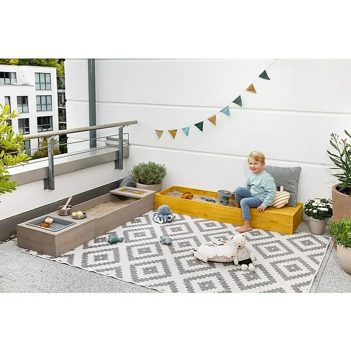Muddy Buddy Sandkasten Flexy Style - 150 x 90 x 20 cm, Holz, Warmgrau/Ocker - Kindersandkästen und Spielküche auf einem Balkon mit dekorativer Wimpelkette, Kissen und Spielzeug für Kinder.