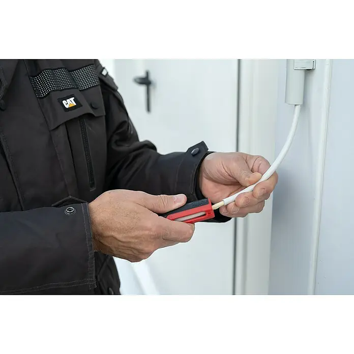 UniTEC Kabelentmanteler - Geeignet für Leitungsquerschnitt: 0,5 mm² - 6 mm² - Nahaufnahme einer Person, die ein CAT-Kabelabisolierwerkzeug verwendet, um ein Kabel vor einer weißen Tür abzumanteln.