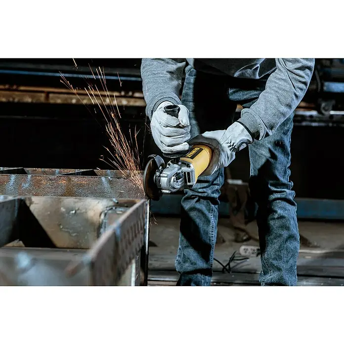 DeWalt Amoladora angular eléctrica DWE4117 - 950 W, Diámetro disco: 125 mm, Número de revoluciones de marcha en vacío: 12.000 r.p.m. - Primer plano de un hombre con ropa de trabajo gris y guantes protectores rectificando metal con una amoladora angular amarilla DeWalt.