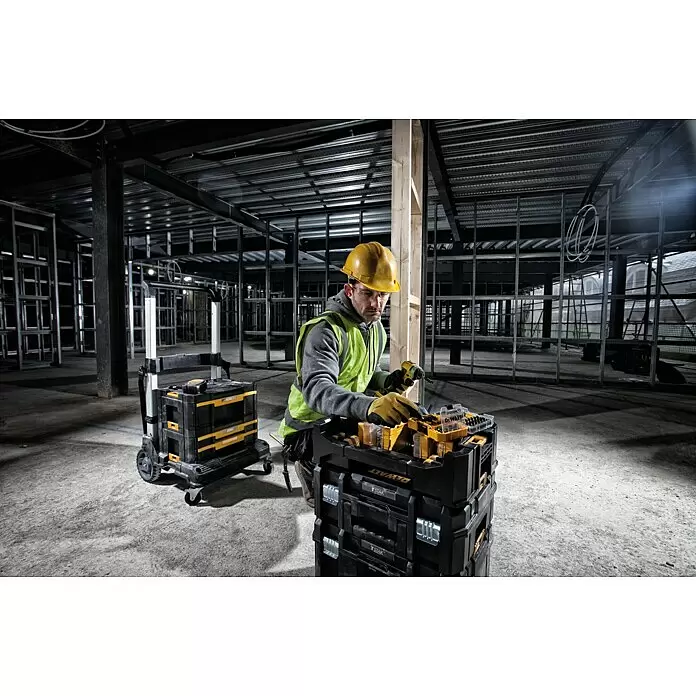 DeWalt Werkzeugkasten - Kunststoff, L x B x H: 437 x 310 x 120 mm - Arbeiter entnimmt Werkzeuge aus schwarzen und gelben gestapelten Dewalt Werkzeugkoffern und einem Rollwagen auf einer Baustelle.