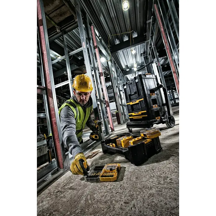 DeWalt Werkzeugkasten - Kunststoff, L x B x H: 437 x 310 x 120 mm - Ein Bauarbeiter mit DeWalt Werkzeug, inklusive Bohrmaschine und Bit-Set, arbeitet an einer Baustelle mit Metallrahmen.