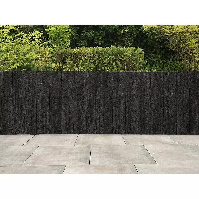 Diephaus Palisade Niles - 90 x 20 x 8 cm, Basalt, Beton - Dunkelgraue, strukturierte Zaunpaneele in einer Außenumgebung, die eine Terrasse von grünem Laub trennen.