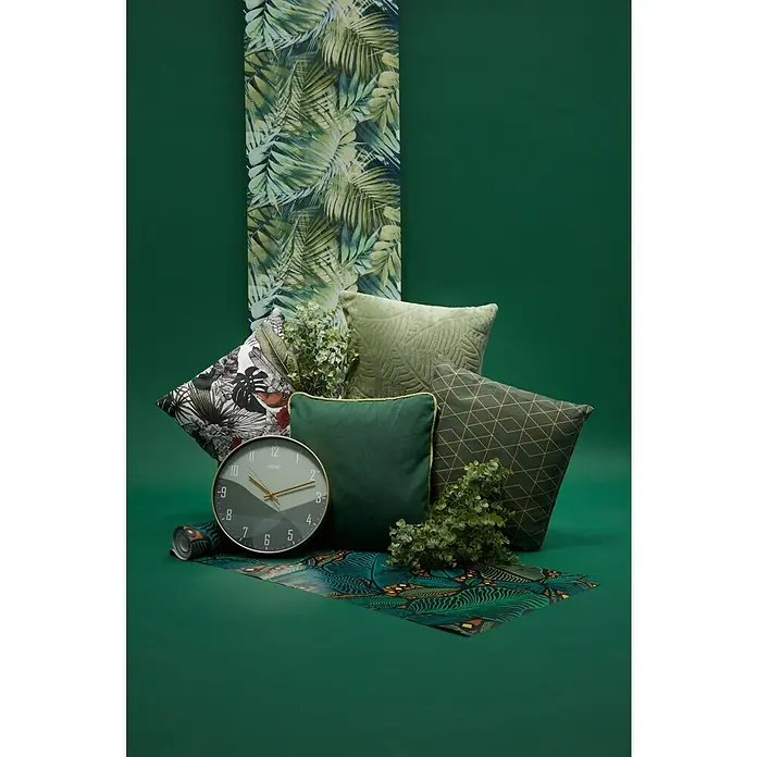Papel pintado Botánico - Azul, Motivo decorativo, 10 x 0,53 m - Primer plano decorativo de cojines verde oscuro, un reloj, plantas y un rollo de papel pintado decorativo sobre un fondo verde oscuro.