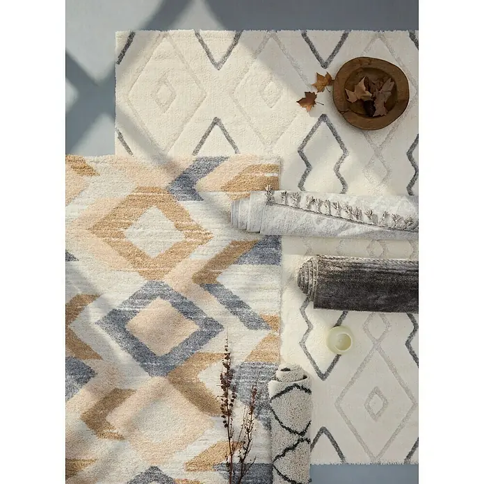 Alfombra de pelo corto Claudia Rombos - Crema, 60 x 110 cm, 100% poliéster - Primer plano de alfombras estampadas variadas en tonos neutros, algunas enrolladas, que muestran textura y variedad de diseño.