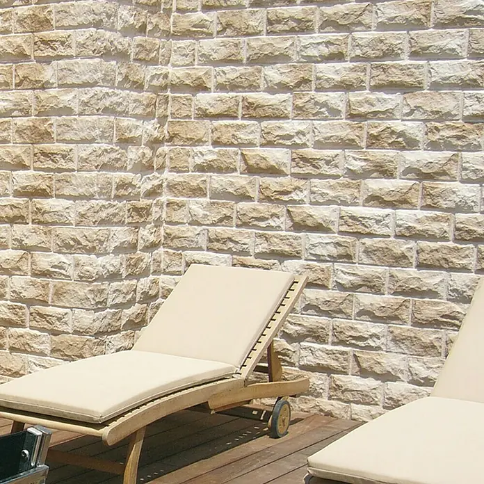 Revestimiento de piedra Teide - 14 x 28 cm, Pardo - Tumbonas con cojines beige en una terraza de madera frente a una pared de piedra clara. Perfecto para relajarse y disfrutar del sol.