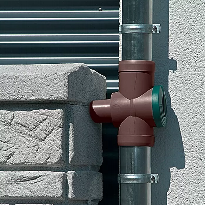 Regensammler Inox - Braun, Grün, Größe Anschluss: 32 mm - Brauner Regenwassersammler aus Kunststoff mit grüner Kappe an einem Fallrohr neben einem Betonpfosten.