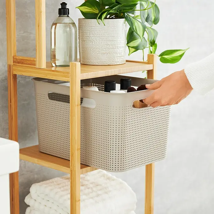 Rotho Aufbewahrungsbox Brisen - L x B x H: 36 x 26,2 x 21,1 cm, Kunststoff, Cappuccino - Ein beiger Aufbewahrungskorb mit Griffen steht in einem Holzregal mit weiteren Badutensilien.