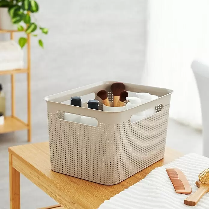 Rotho Aufbewahrungsbox Brisen - L x B x H: 36 x 26,2 x 21,1 cm, Kunststoff, Cappuccino - Hellbrauner, perforierter Kunststoff-Aufbewahrungskorb mit Flaschen und Bürsten auf einer Holzoberfläche.