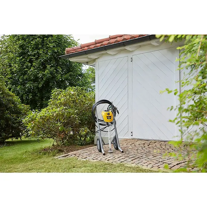 Wagner High Efficiency Airless Farbsprühsystem Control Pro 350 M - 600 W, Arbeitsgeschwindigkeit: 7,5 m²/min - Diese Aufnahme zeigt eine Farbspritzmaschine im Freien vor einem Schuppen. Sie ist gelb und hat einen schwarzen Schlauch.