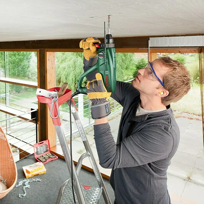 Bosch Kombihammer PBH 2200 RE - 570 W, 1,8 J, SDS-Plus-Aufnahme - Mann bohrt mit einer grünen Bosch-Bohrmaschine ein Loch in die Decke, um etwas zu installieren. Er steht auf einer Leiter.