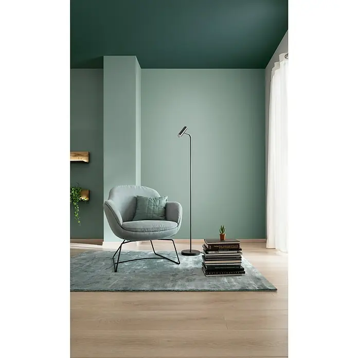 SCHÖNER WOHNEN-Farbe Wandfarbe TrendfarbeJungle, Matt, 2,5 l, Konservierungsmittelfrei - Einrichtungsidee mit modernem Sessel, Stehlampe und einem Stapel Bücher auf einem flauschigen Teppich. Die mintgrünen Wände schaffen eine ruhige Atmosphäre.