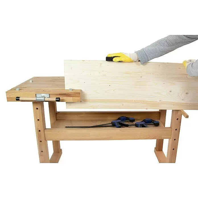 Rikta Hobelbank - L x B: 140 x 50 cm, Arbeitshöhe: 83 cm, Holz - Person in gelben Handschuhen schleift ein großes Holzbrett, das in einer hellen Holzwerkbank mit Schraubstock eingespannt ist. Zwingen liegen auf der Ablage.