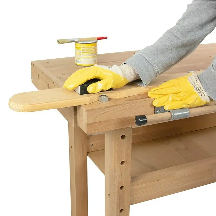 Rikta Hobelbank - L x B: 140 x 50 cm, Arbeitshöhe: 83 cm, Holz - Nahaufnahme eines Holzarbeiters, der ein Holzstück mit Schleifpapier auf einer Werkbank schleift. Werkbank mit Zubehör wie Pinsel und Farbdose.