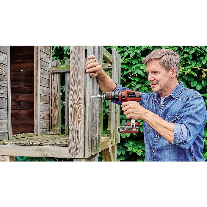 Einhell PXC 18V Taladro atornillador de batería TE-CD18/45 - 18 V, 2 baterías, 2 Ah, 45 Nm - Un hombre usa un taladro inalámbrico Einhell para construir una caseta de madera. El taladro es rojo y negro y tiene una batería.