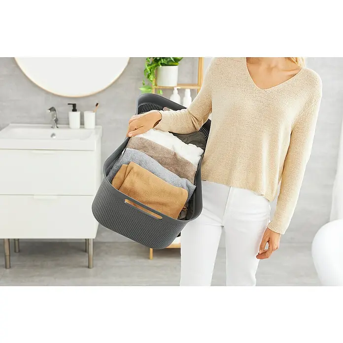 Rotho Wäschekorb Brisen - L x B x H: 59,6 x 39,6 x 23,2 cm, Kunststoff, Anthrazit - Eine Person trägt einen grauen Wäschekorb mit gefalteter Kleidung. Ideal für die Organisation und Aufbewahrung von Wäsche im Badezimmer.