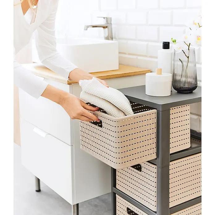 Rotho Rollenaufbewahrungsbox Country - L x B x H: 37,5 x 37,5 x 71,2 cm, Cappuccino - Frau räumt weiße Handtücher in einen beigefarbenen Aufbewahrungskorb im Badezimmer. Praktische Badmöbel zur Aufbewahrung von Handtüchern.