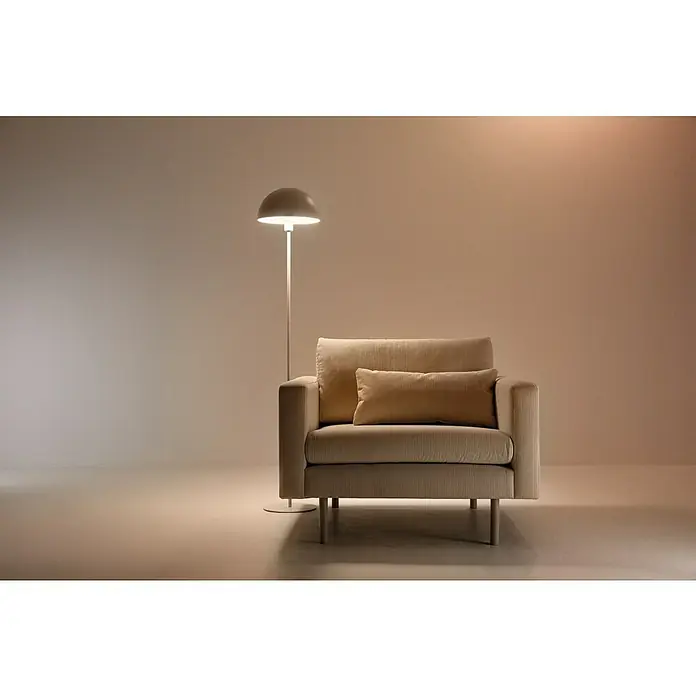 Philips Wiz Bombilla LED inteligente Full color - E27, RGBW, 806 lm, 8,5 W - Interior elegante con un sillón beige y una lámpara de pie, que emite una luz cálida y acogedora. El sillón está diseñado para la relajación.