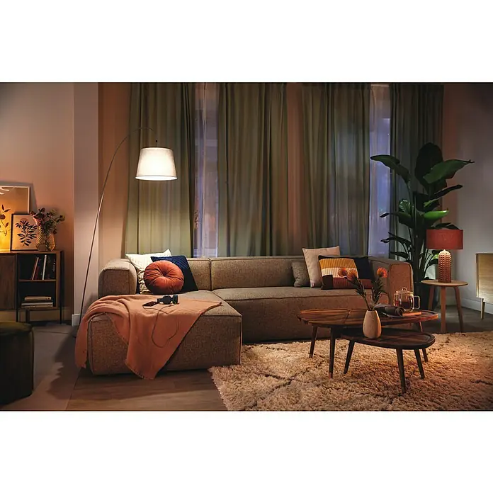 Philips Wiz Bombilla LED inteligente Full color - E27, RGBW, 806 lm, 8,5 W - Sala de estar con un sofá seccional beige, lámpara de pie y mesa de centro sobre una alfombra mullida.