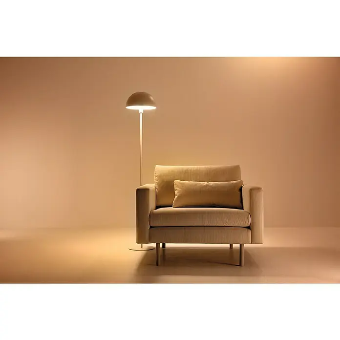 Philips Wiz Bombilla LED inteligente Full color - E27, RGBW, 806 lm, 8,5 W - Una escena acogedora con un sillón beige y una lámpara de pie que emite una luz cálida. Ideal para relajarse y leer en el cómodo sillón.