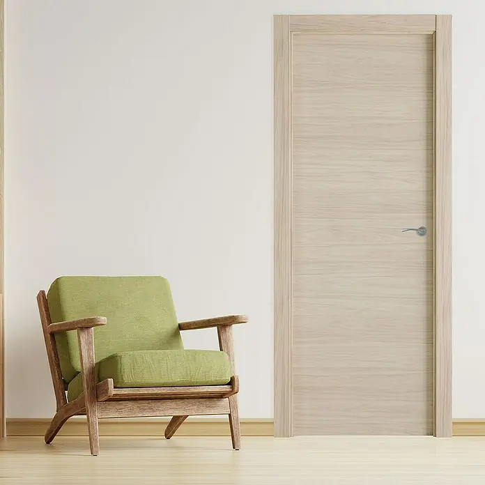 Pack puerta de interior Arizona - 82,5 x 203 cm, Izquierda, Roble arena - Una puerta de madera clara moderna con un diseño minimalista se encuentra junto a un sillón verde, aportando un ambiente tranquilo a la habitación.