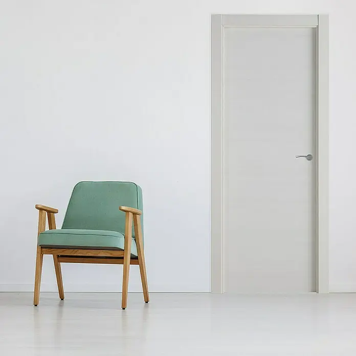 Pack puerta de interior Nebraska - 82,5 x 203 cm, Izquierda, Gris claro - Interior acogedor con un sillón verde menta junto a una elegante puerta blanca, realzando la estética de diseño moderno de la habitación.