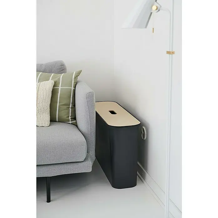 SmartStore Collect Mülltrennsystem Slim - 46 l, Schwarz, Rechteckig, Kunststoff - Seitenansicht eines modernen, schmalen Nachttisches in Schwarz und Beige, der neben einem grauen Sofa steht.