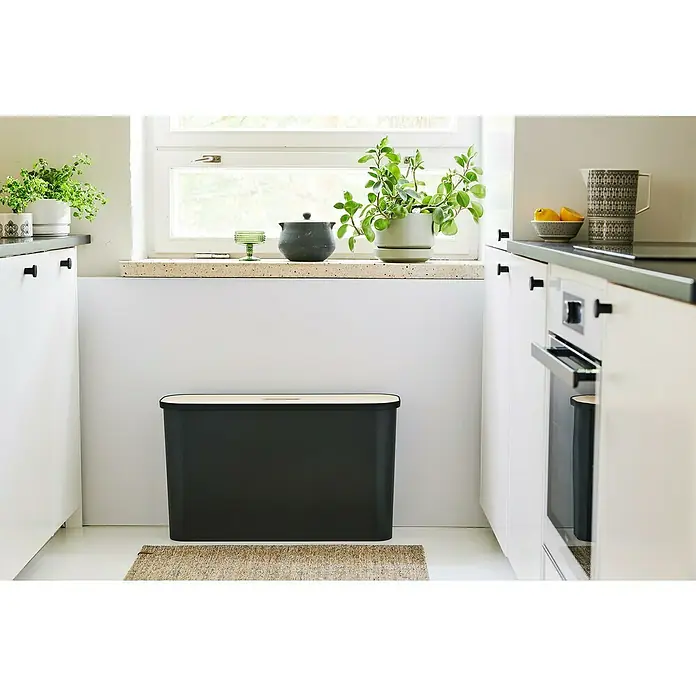 SmartStore Collect Mülltrennsystem Slim - 46 l, Schwarz, Rechteckig, Kunststoff - Ein stilvoller, schwarzer Brotkasten mit einem Holzdeckel steht in einer modernen Küche auf einem beigen Teppich.