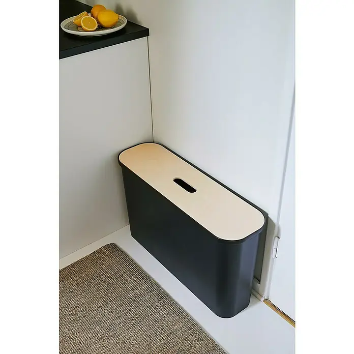 SmartStore Collect Mülltrennsystem Slim - 46 l, Schwarz, Rechteckig, Kunststoff - Schwarzer Papierkorb mit Holzdeckel, der in einer Ecke neben einer Fußmatte in einem Raum steht.