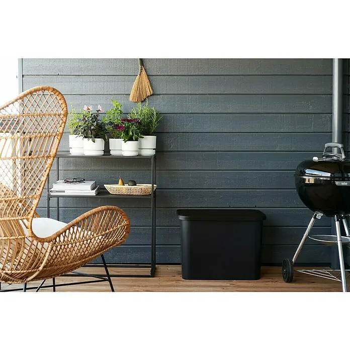 SmartStore Collect Deckel - 40 x 58,5 cm, Kunststoff, Schwarz - Ein gemütlicher Außenbereich mit einem stilvollen Rattansessel, Pflanzen auf einem Regal und einem schwarzen Grill.