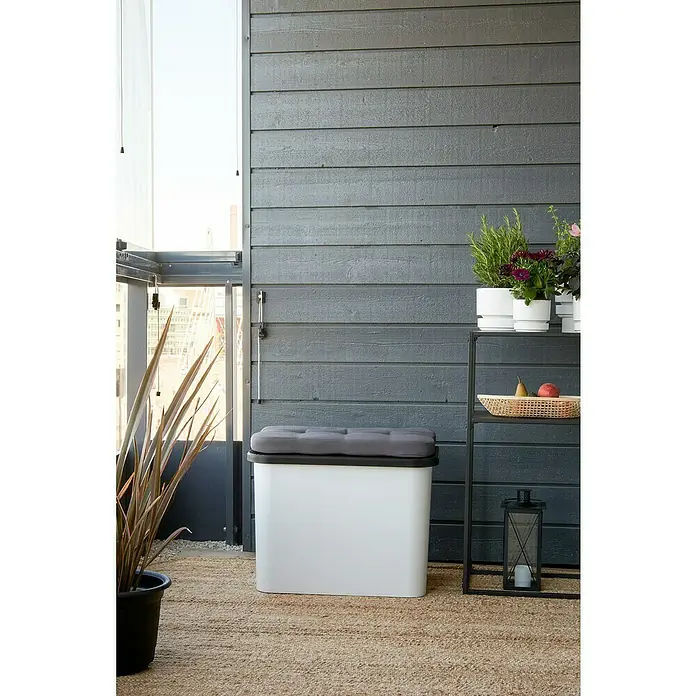 SmartStore Collect Deckel - 40 x 58,5 cm, Kunststoff, Schwarz - Ein weißer Aufbewahrungskasten mit grauem Kissenauflage steht auf einem Teppich, neben einem schwarzen Regal auf einer Terrasse.