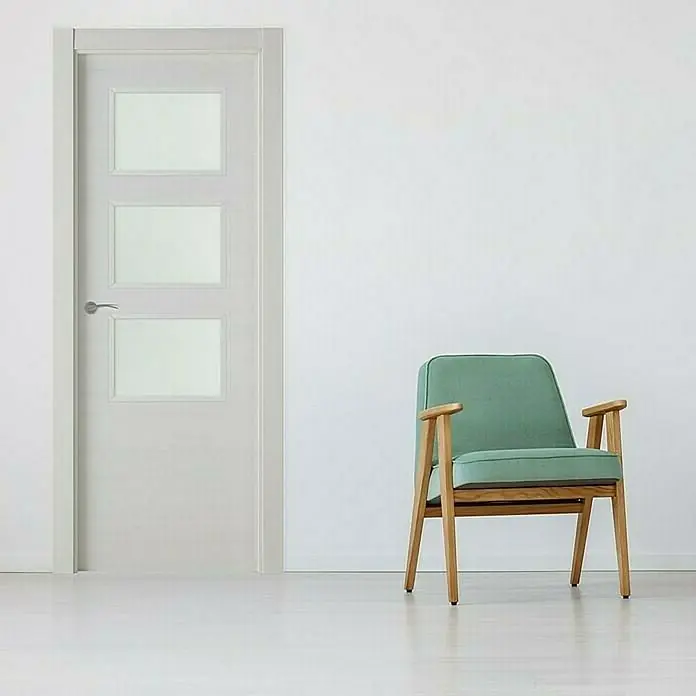 Pack puerta acristalada Nebraska - 82,5 x 203 cm, Derecha, Gris claro - Una puerta blanca moderna con tres paneles de vidrio junto a un sillón color menta en una habitación luminosa.