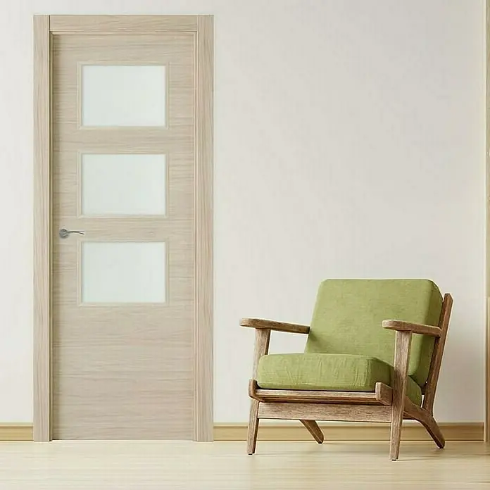 Pack puerta acristalada Arizona - 72,5 x 203 cm, Derecha, Roble arena - Puerta de madera clara con tres inserciones cuadradas de vidrio y manija moderna, al lado de un sillón verde sobre piso de madera.