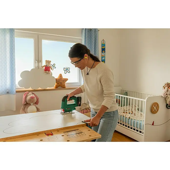 Bosch Power for All 18V Akku-Stichsäge EasySaw 18V-70 - 18 V, 1 Akku, 2 Ah, Leerlaufhubzahl: 2.600 /min - Frau arbeitet mit einer Bosch Stichsäge an einem DIY-Projekt im Kinderzimmer. Schutzbrille und Ohrstöpsel sind getragen.
