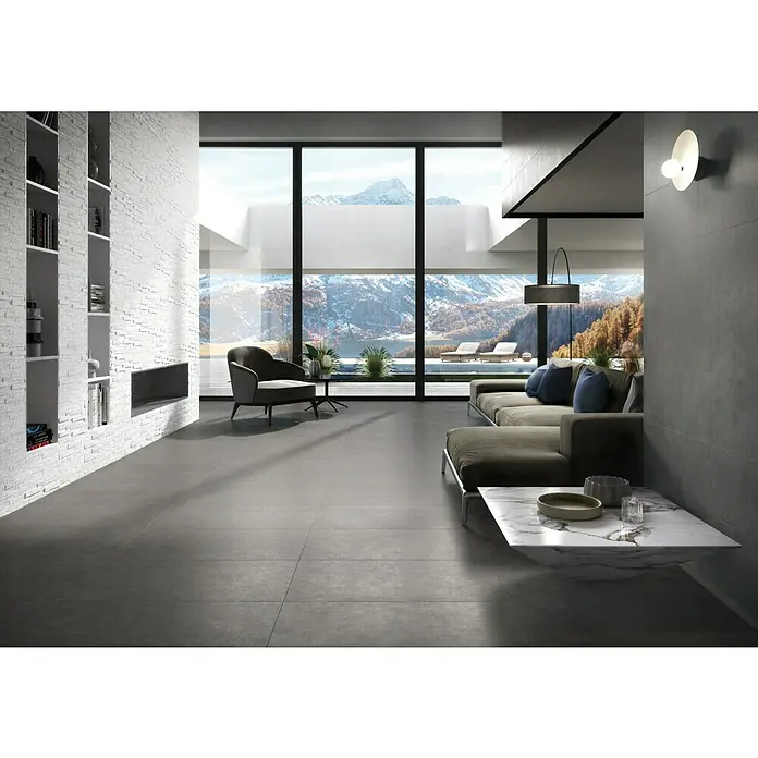 Ambiente by Palazzo Feinsteinzeugfliese30 x 60 cm, Grau, Matt - Das Bild zeigt einen modernen Wohnraum mit grauen Fliesen, einem Sofa und einem Tisch. Die großen Fenster bieten einen Blick auf eine schneebedeckte Berglandschaft.
