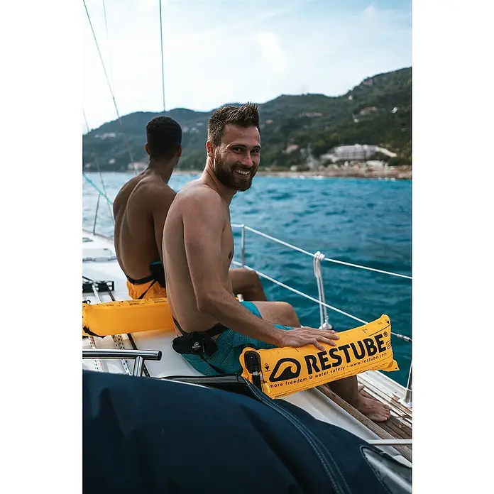 Restube Rettungsboje Restube beach - Geeignet für: 1 Person, Gelb - Das Bild zeigt zwei Männer mit RESTUBE-Schwimmhilfen auf einem Boot. Die gelben RESTUBEs bieten Sicherheit und Freiheit beim Wassersport.