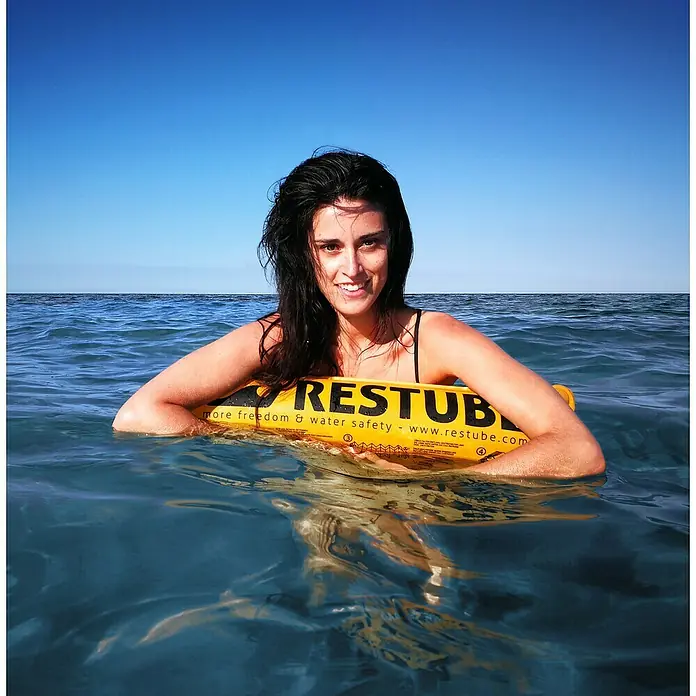 Restube Rettungsboje Restube beach - Geeignet für: 1 Person, Gelb - Eine Frau schwimmt im Wasser und hält einen gelben Restube Schwimmkörper fest, der für mehr Freiheit und Wassersicherheit sorgt.
