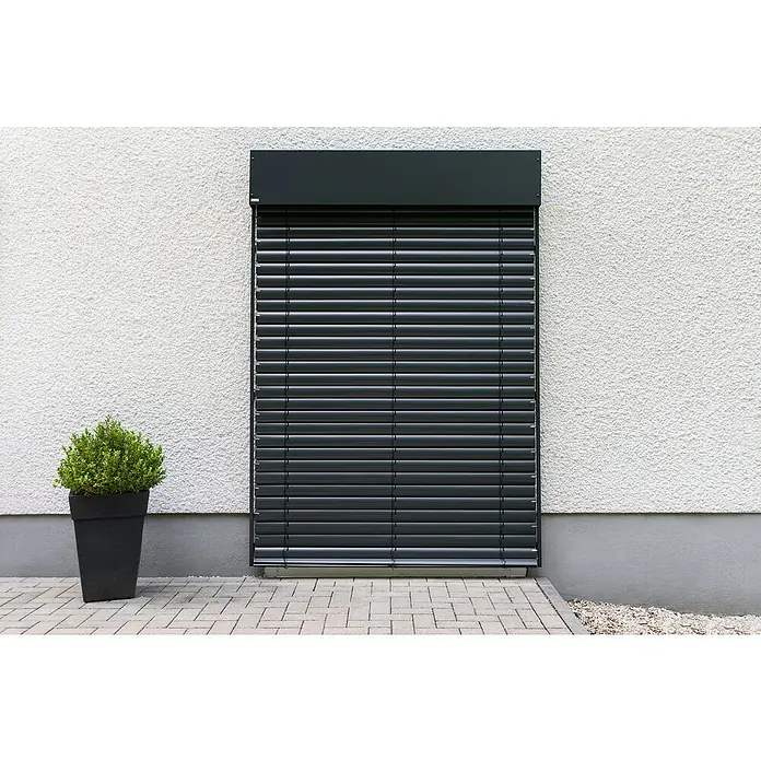 Schellenberg Raffstore Express - 170 x 160 cm - Aufnahme einer geschlossenen, grauen Außenjalousie an einer Fassade, die das Fenster abdeckt und für Schatten sorgt. Ein grüner Busch steht davor.