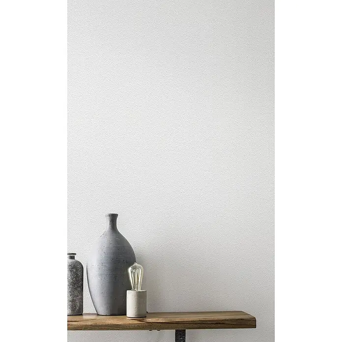Rasch Vliestapete Feel Good - Weiß, Uni, 10,05 x 0,53 m, Grobe Struktur - Graue Keramikvasen und eine Lampe mit einer Edison-Glühbirne stehen auf einem Holztisch vor einer weißen Wand.