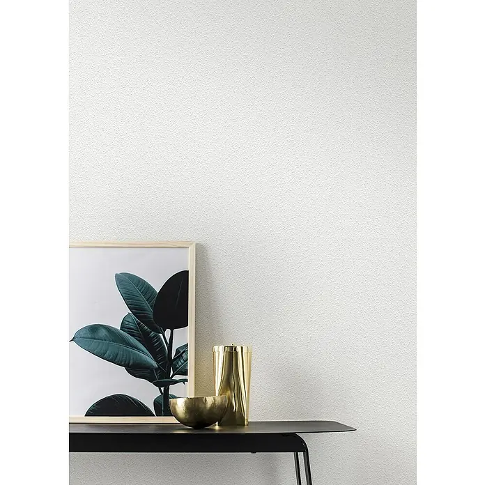 Rasch Wallton Vliestapete Feel Good Vlies-Raufasertapete - Weiß, Uni, 10,05 x 0,53 m - Nahaufnahme eines weißen Wandbildes mit dezenter Textur, daneben ein Bild und goldene Accessoires auf einem schwarzen Tisch.