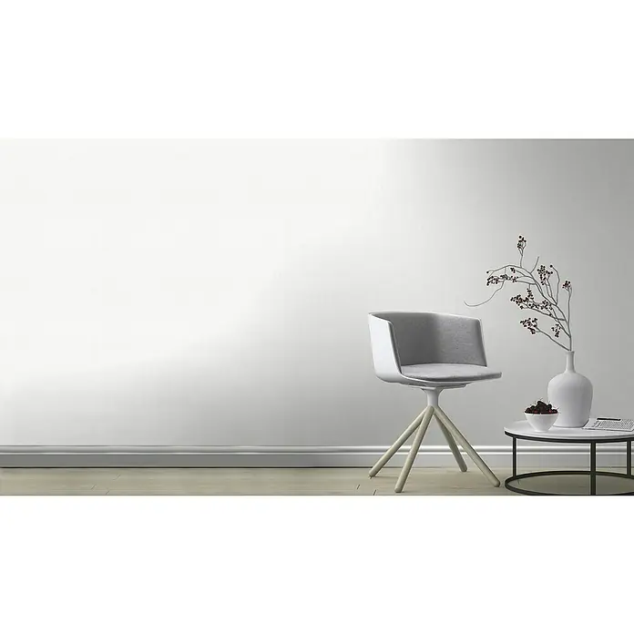 Rasch Wallton Vliestapete Feel Good - Weiß, Uni, 10,05 x 0,53 m - Elegantes Interieur mit einem modernen, grauen Drehstuhl auf einem hellen Holzboden, neben einem Tisch mit stilvoller Dekoration vor einer weißen Wand.