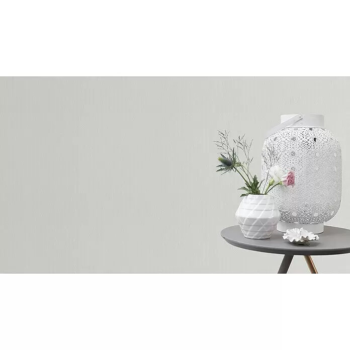 Rasch Vliestapete Feel Good - Weiß, Uni, 10,05 x 0,53 m, Längsstruktur - Weiße Dekolaterne, strukturierte Vase mit Blumen und eine Muschelschale auf einem grauen Beistelltisch.