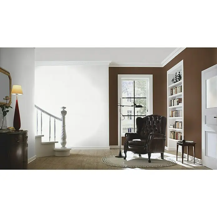 Rasch Vliestapete Feel GoodWeiß, Uni, 10,05 x 0,53 m, Längsstruktur - Eine Leseecke mit einem braunen Ledersessel, einer Stehlampe und einem Bücherregal in einem gemütlichen Raum mit Holzboden.
