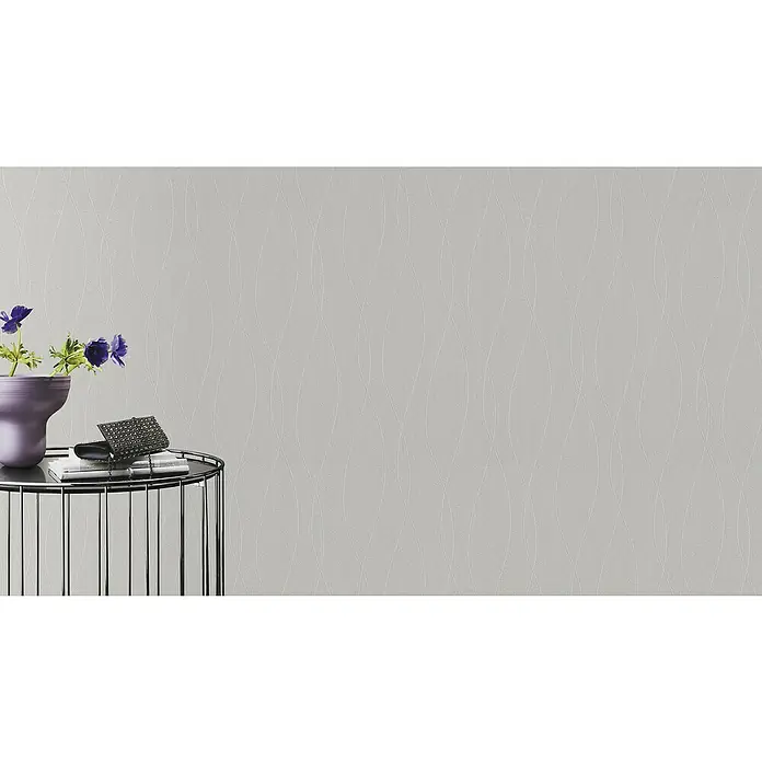 Rasch Wallton Vliestapete Feine Putzstruktur - Weiß, Wellen, 25 x 1,06 m - Nahaufnahme eines stilvollen Beistelltisches mit Blumen, Buch und Clutch vor einem gemusterten, grauen Hintergrund.