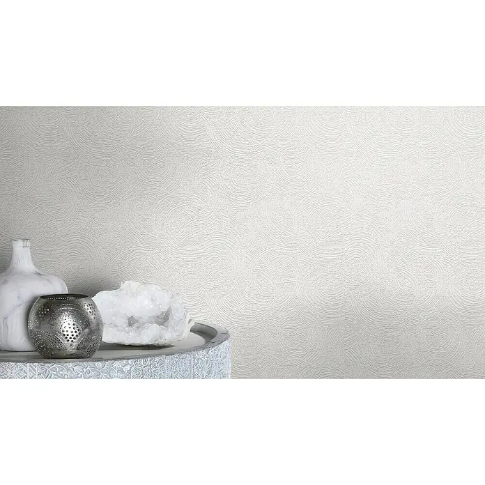 Rasch Wallton Vliestapete Premium Kreise - Weiß, Grafisch, 10,05 x 0,53 m - Nahaufnahme von drei dekorativen Objekten: einer weißen Vase, einem silbernen Teelichthalter und einem weißen Kristall auf einem verzierten Tisch.