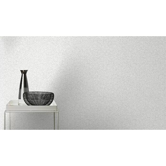 Rasch Wallton Vliestapete Putzstruktur - Weiß, Uni, 10,05 x 0,53 m, Grobe Struktur, Matt - Texturierte weiße Tapete bedeckt eine Wand in einem Raum, mit Dekorationsartikeln auf einem Tisch zur Skalierung.