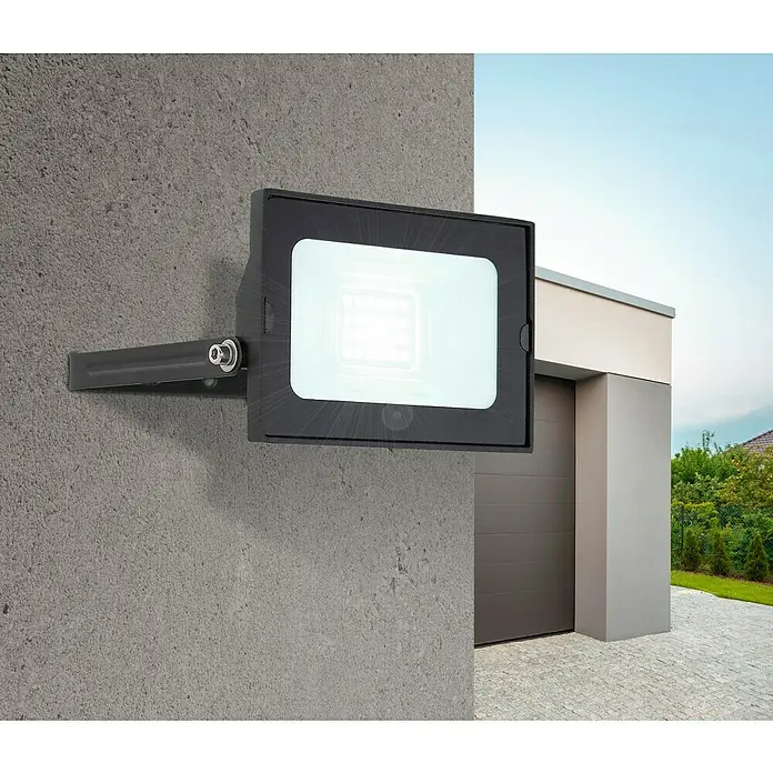 Globo LED-Strahler Helga - 20 W, Schwarz, Kaltweiß - Nahaufnahme eines schwarzen LED-Strahlers an einer grauen Wand mit einem modernen Haus im Hintergrund.