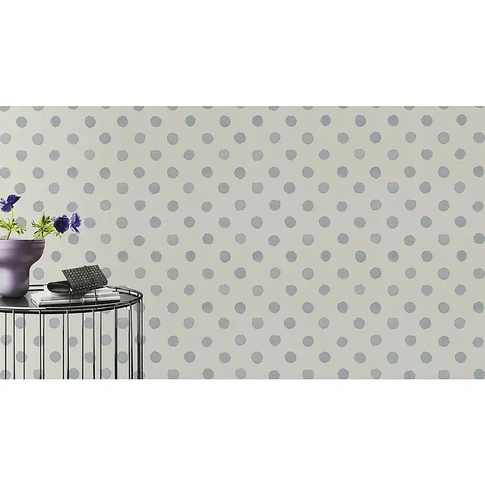 Rasch Bambino XIX Vliestapete Punkte - Blau, Grafisch, 10,05 x 0,53 m - Nahaufnahme eines Beistelltisches mit Blumen und Accessoires, vor einem Hintergrund mit grauen Tupfen. Das Arrangement strahlt Eleganz und Stil aus.